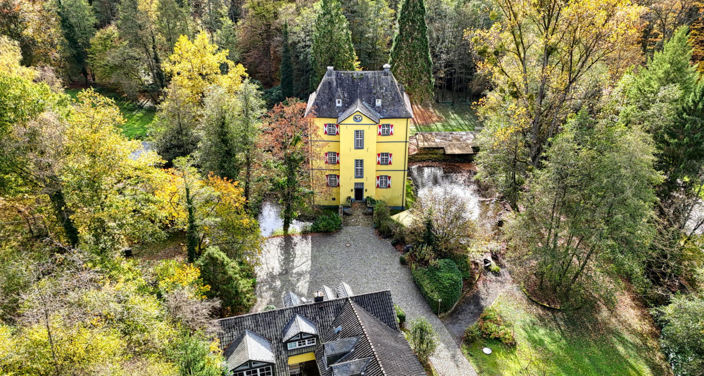 Drohnenaufnahme eines historischen Herrenhauses mit Wassergraben im herbstlichen Rheinland